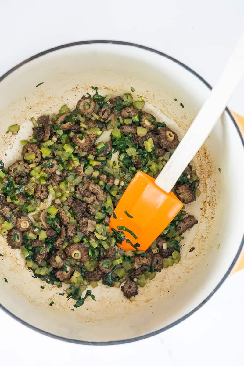 morels, ramps and celery sautéed in butter with a orange rubber spatula in a dutch oven