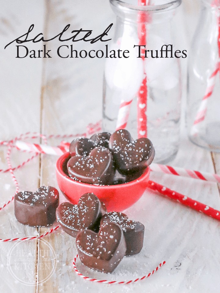 heart shaped dark chocolate truffles in a red bowl topped with sea salt on a white wooden background