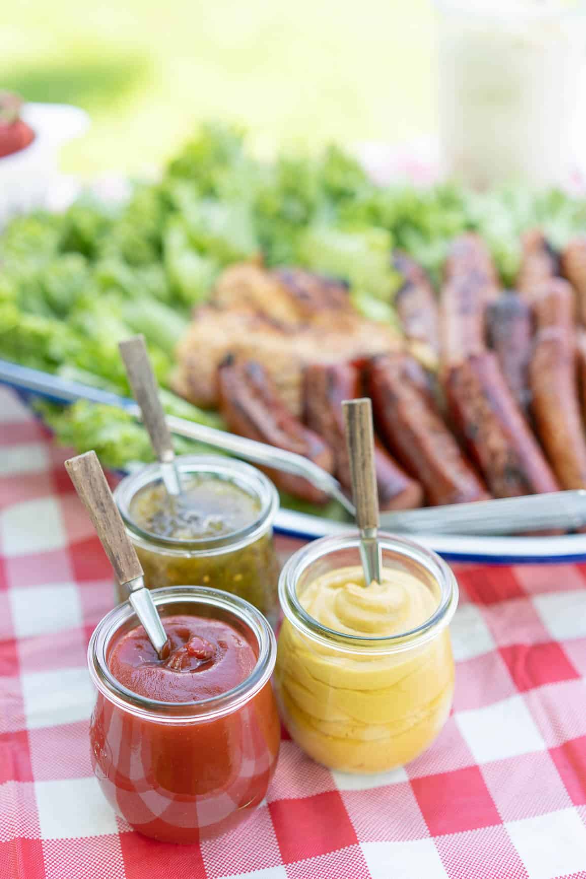 ketchup, mustard and relish in weck jars with spoons on a picnic table
