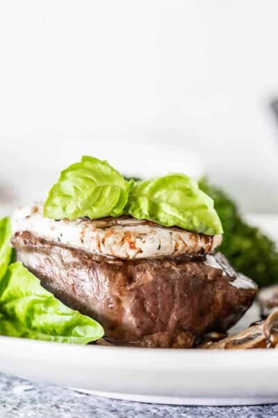 Petite filet topped with goat cheese and basil on a white plate