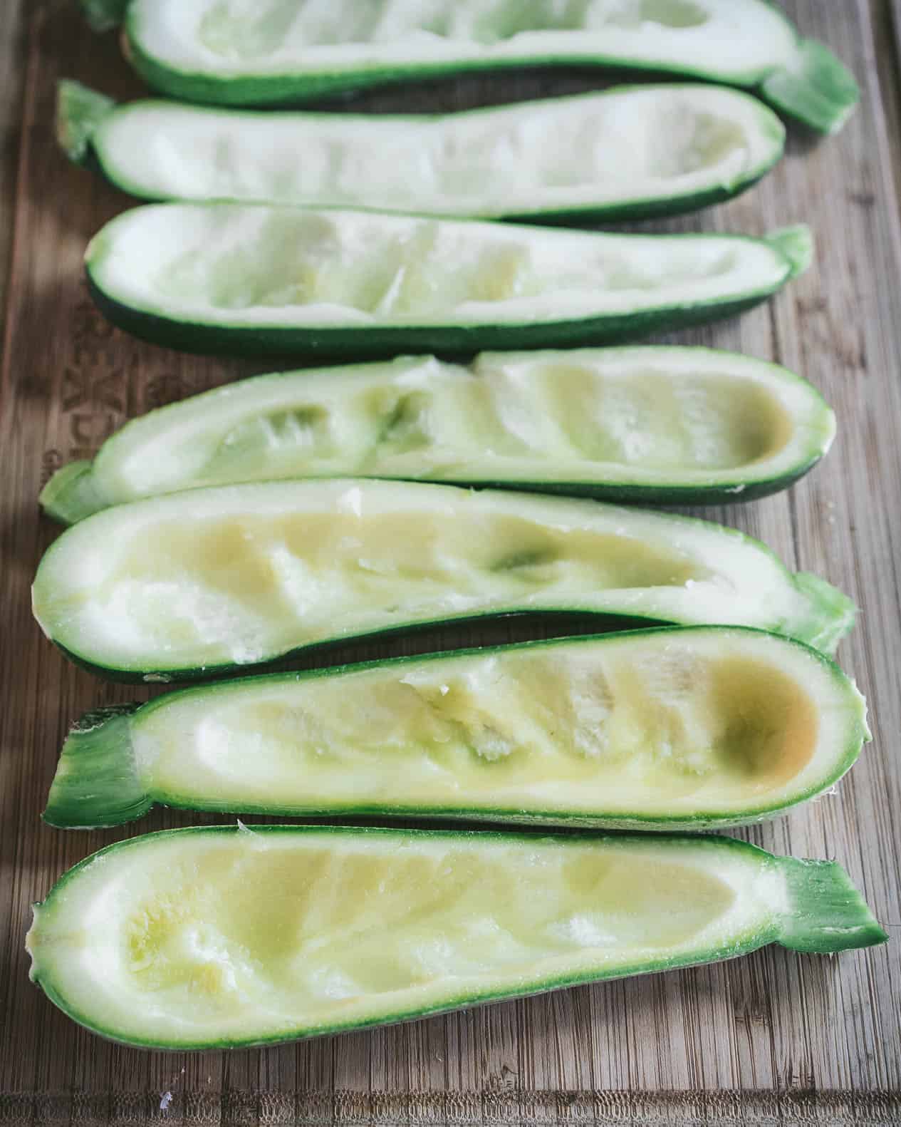 zucchini halves with the seeds scooped out to make boats on a wooden cutting board.