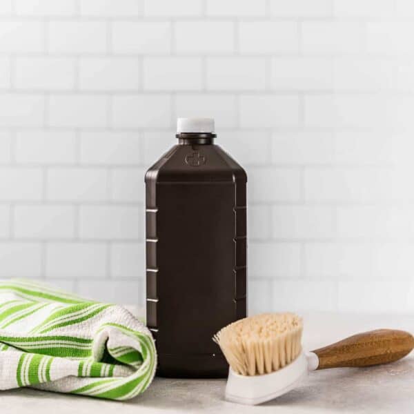 Bottle of hydrogen peroxide in front of a white subway tile wall with green stripe kitchen towel and cleanign brush