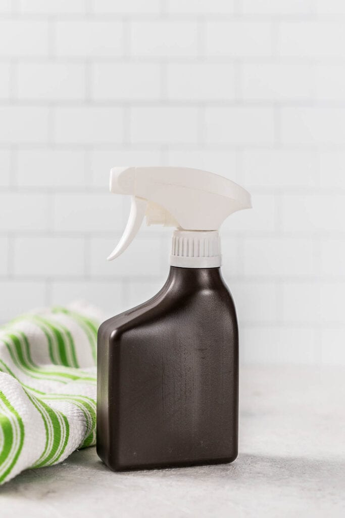 spray bottle of hydrogen peroxide in front of a white subway tile wall with green stripe kitchen towel on left