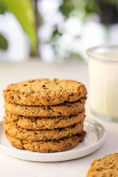 stack of 5 chocolate chip cookies with a cookie in the front with a bite taken out, glass of milk in the background