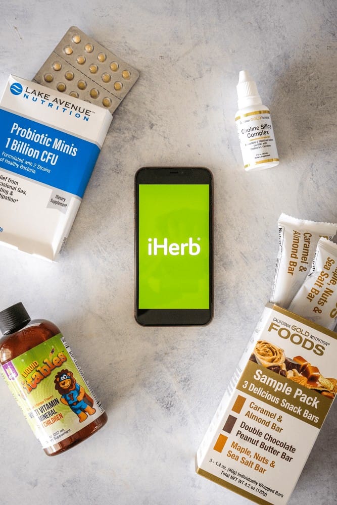 Image of the green iherb logo on a iPhone 11 pro with products surrounding. 