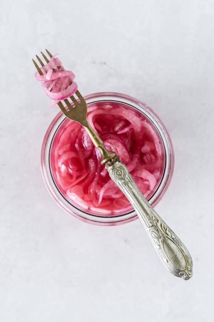pickled red onions in a jar and coiled on a fork