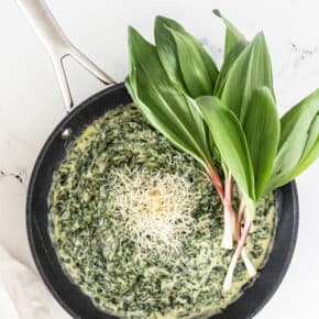 Creamed Ramp Greens in a non stick skillet, garnished with shredded cheese and fresh whole ramps