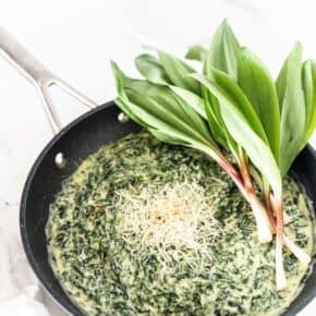 Creamed Ramp Greens in a non stick skillet, garnished with shredded cheese and fresh whole ramps