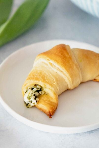 Ramp stuffed crescent on a white plate with whole, wild ramps on the left side. blue background