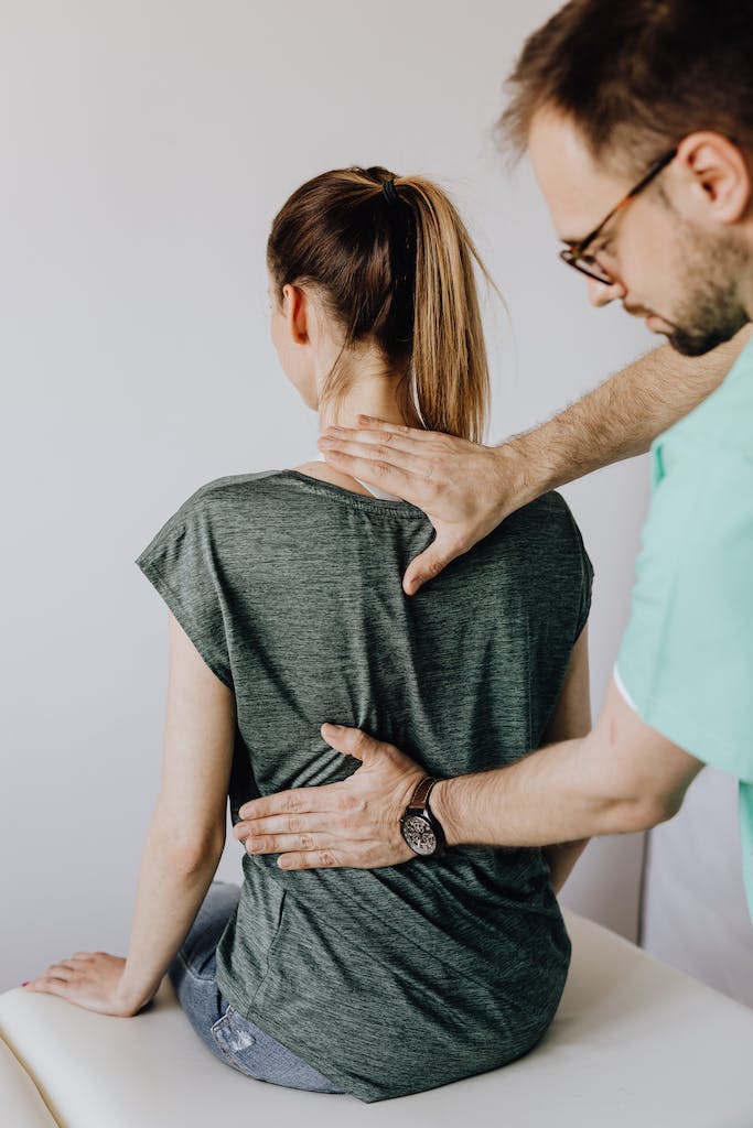 Crop osteopath examining back of anonymous woman in doctor office