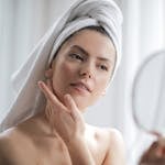Selective Focus Portrait Photo of Woman With a Towel on Head Looking in the Mirror