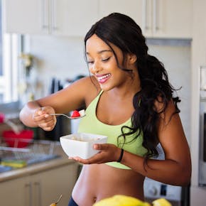 Cheerful woman enjoying fresh strawberries in a cozy kitchen setting. Promotes healthy living and happiness.