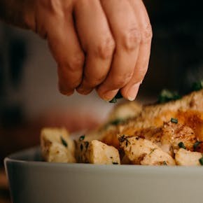 Close-up of a chef's hand garnishing roasted potatoes with herbs, enhancing culinary presentation.
