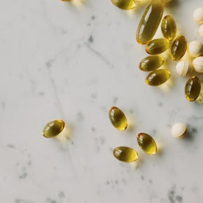 Close-up of assorted gel capsules and pills scattered on a marble surface, suggesting health and wellness.