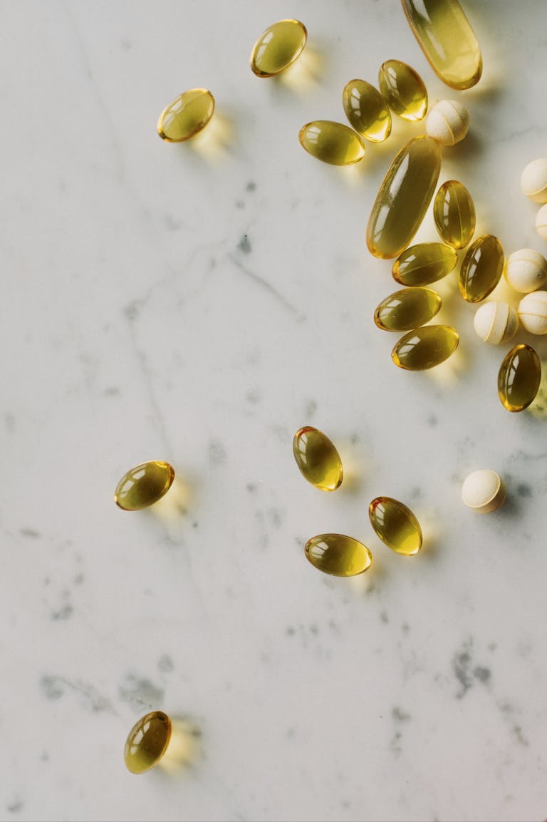 Close-up of assorted gel capsules and pills scattered on a marble surface, suggesting health and wellness.