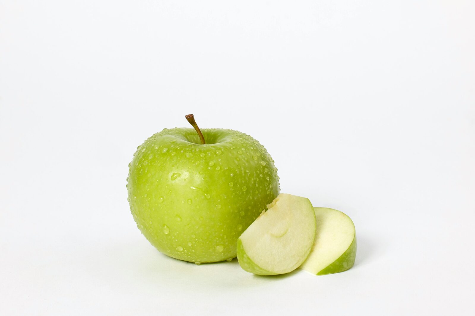 a green apple with water drops next to a slice of apple