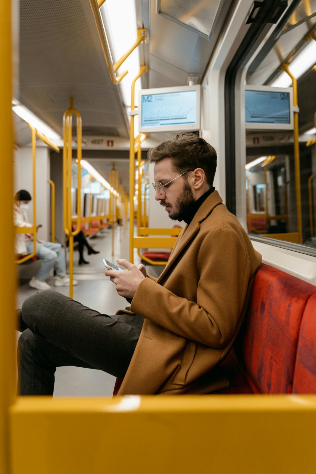 Caucasian man sitting on train seat, focused on smartphone use during a daytime commute.
