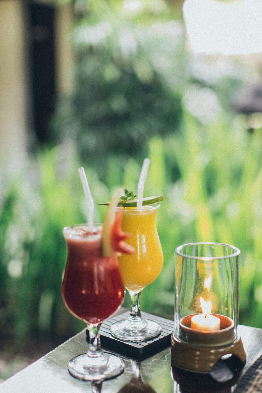 Vibrant cocktails adorned with straws on a table beside a glowing candle.