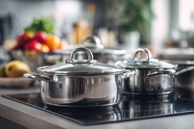 Stainless steel cookware on a modern stovetop. Fresh produce in the background
