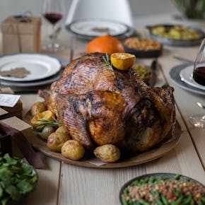 High angle of appetizing roasted turkey and glasses of wine with other dishes placed on wooden table prepared for celebrating Thanksgiving Day