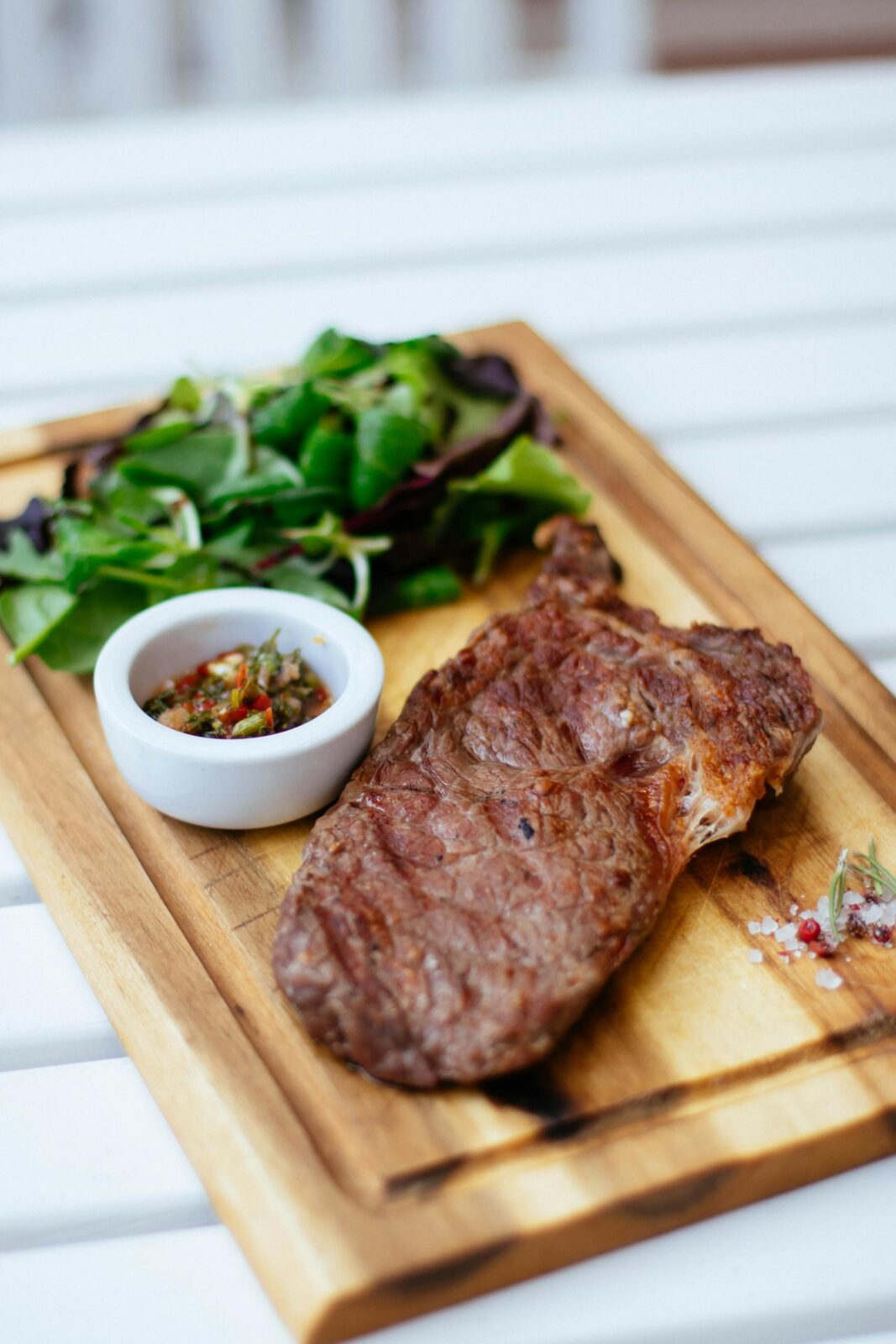Juicy grilled steak served with fresh herb salad and sauce on a wooden board.