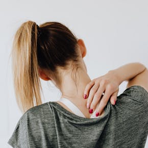 A woman in casual clothing holds her neck, indicating pain or discomfort.
