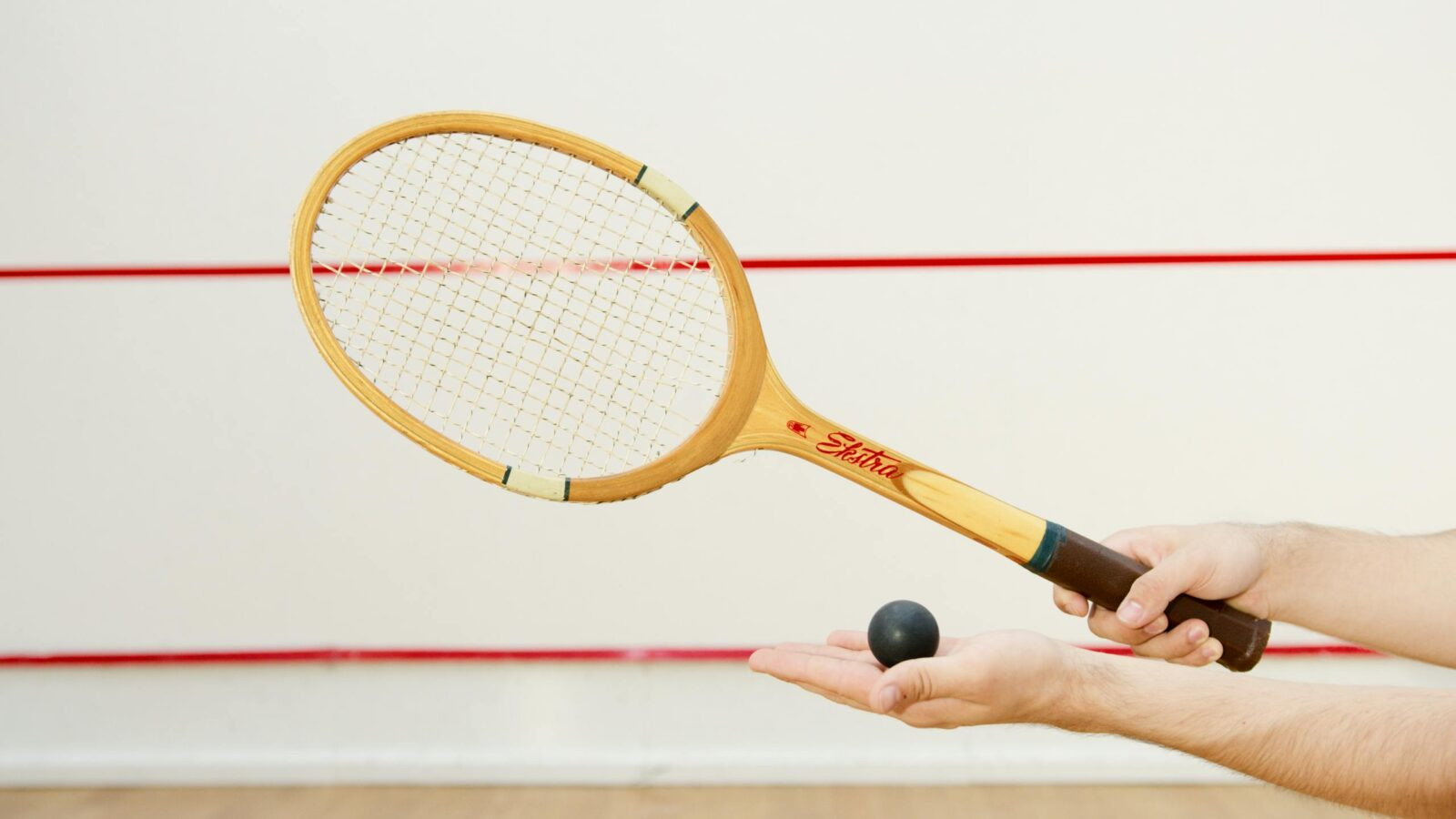 Detailed view of a squash racket and ball in hand, indoor sports scene.