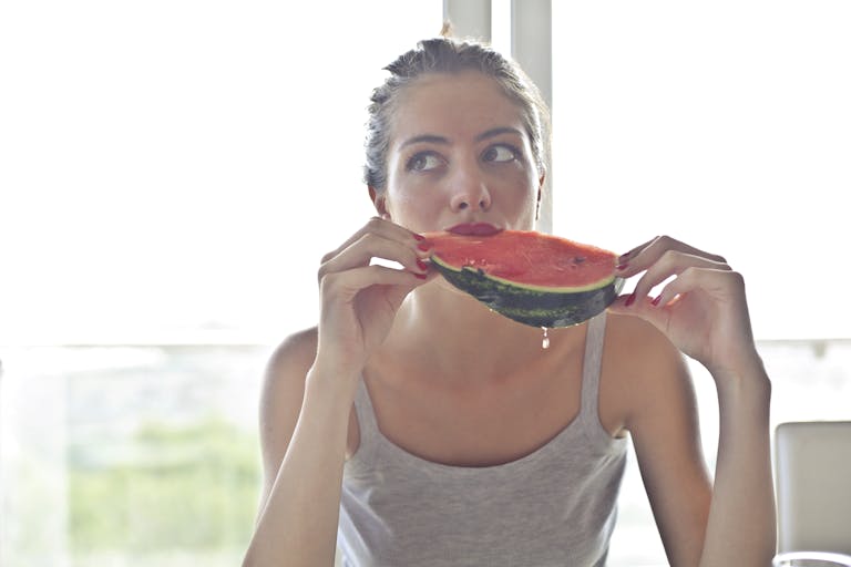 Portrait of a woman eating watermelon indoors, reflecting health and summer vibes.