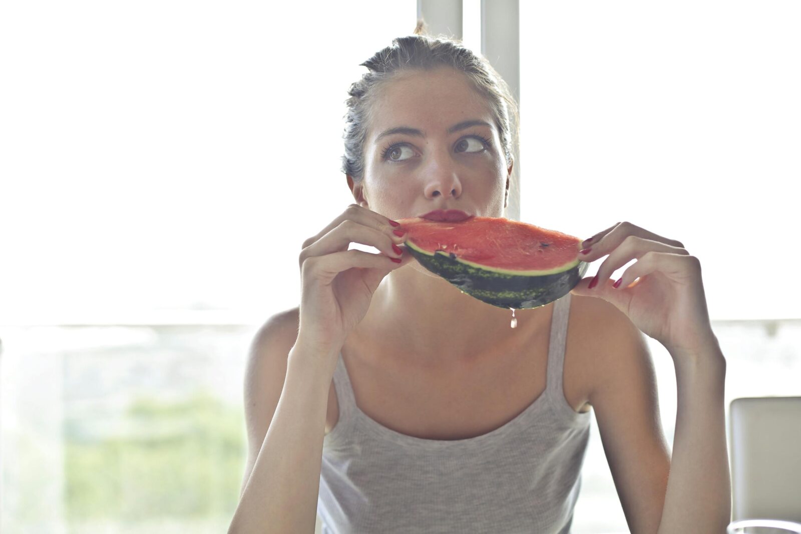 Portrait of a woman eating watermelon indoors, reflecting health and summer vibes.