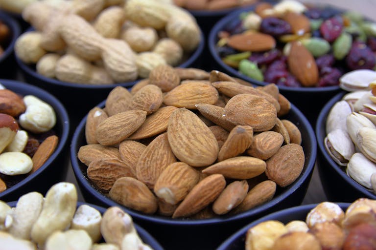 Collection of assorted nuts and dried fruits in black bowls, showcasing colorful and healthy snacks.
