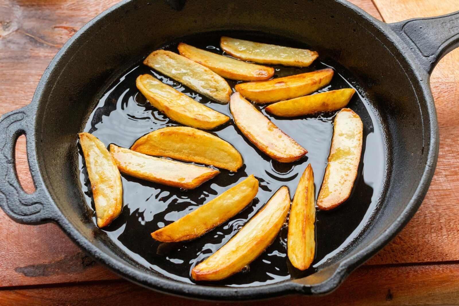 Freshly fried golden potato wedges sizzling in a cast iron skillet, showcasing delicious homemade cooking.
