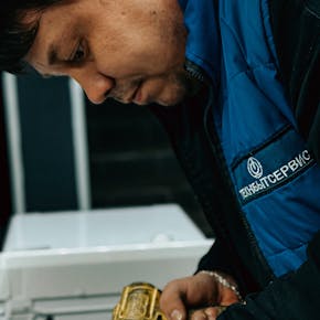 Technician in blue jacket using a power drill indoors for maintenance.