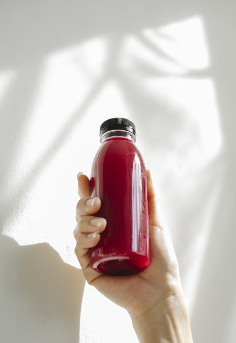 A hand holding a refreshing red juice bottle against a white background, conveying health and freshness.