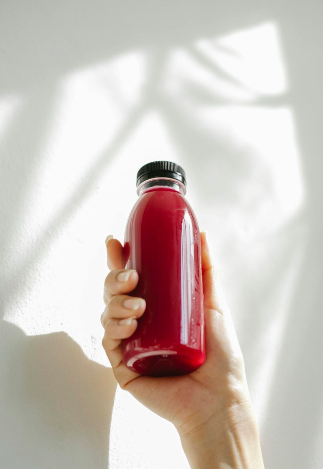 A hand holding a refreshing red juice bottle against a white background, conveying health and freshness.