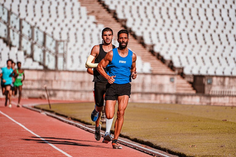 Focused male runners competing on a sports track during a daytime race in a stadium setting.