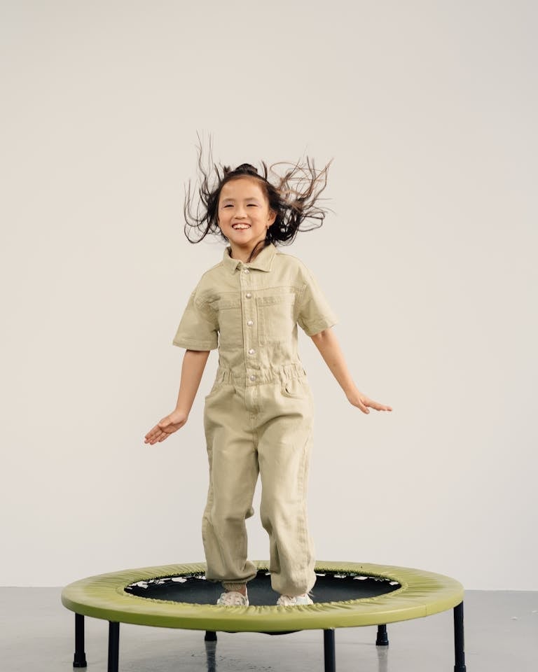 Joyful young girl jumping on a trampoline with a playful smile, showcasing fun and energy.