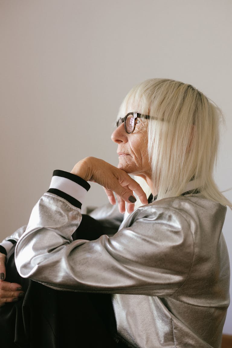 Side view of a pensive elderly woman in a shiny jacket looking thoughtful indoors.
