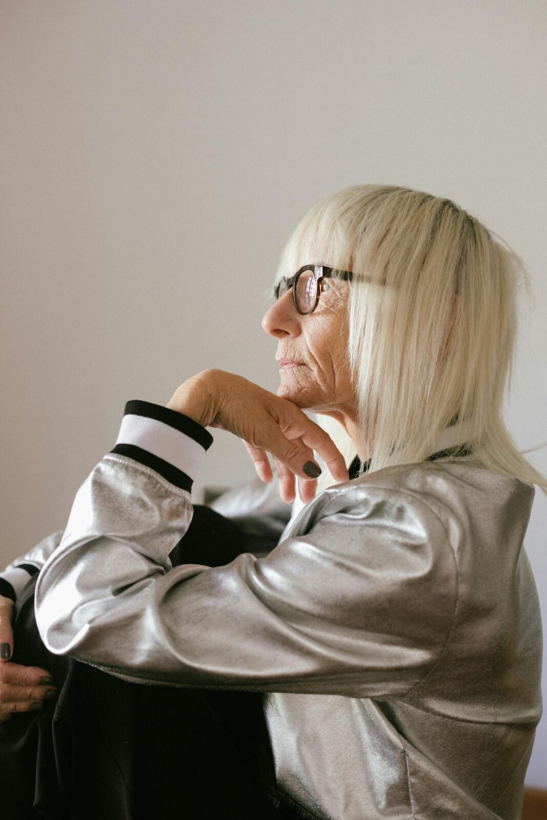 Side view of a pensive elderly woman in a shiny jacket looking thoughtful indoors.