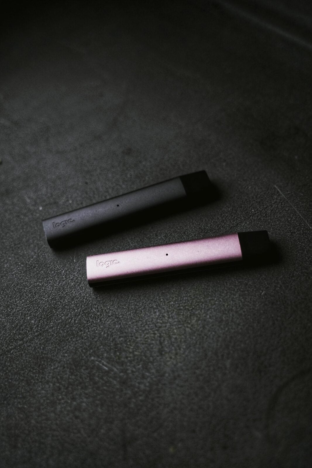 Two sleek vape devices in pink and black on a textured dark background.