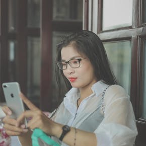 Young Asian woman touching smartphone screen indoors for communication and entertainment.