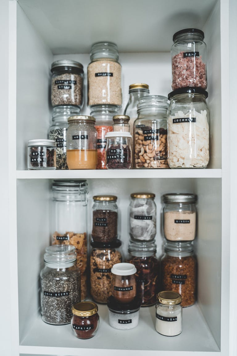 Clean pantry shelves displaying various food items stored in labeled glass jars.