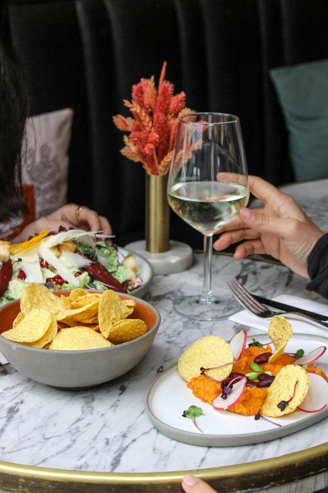 Close-up of a stylish dining setup with wine, salads, and appetizers in a restaurant.