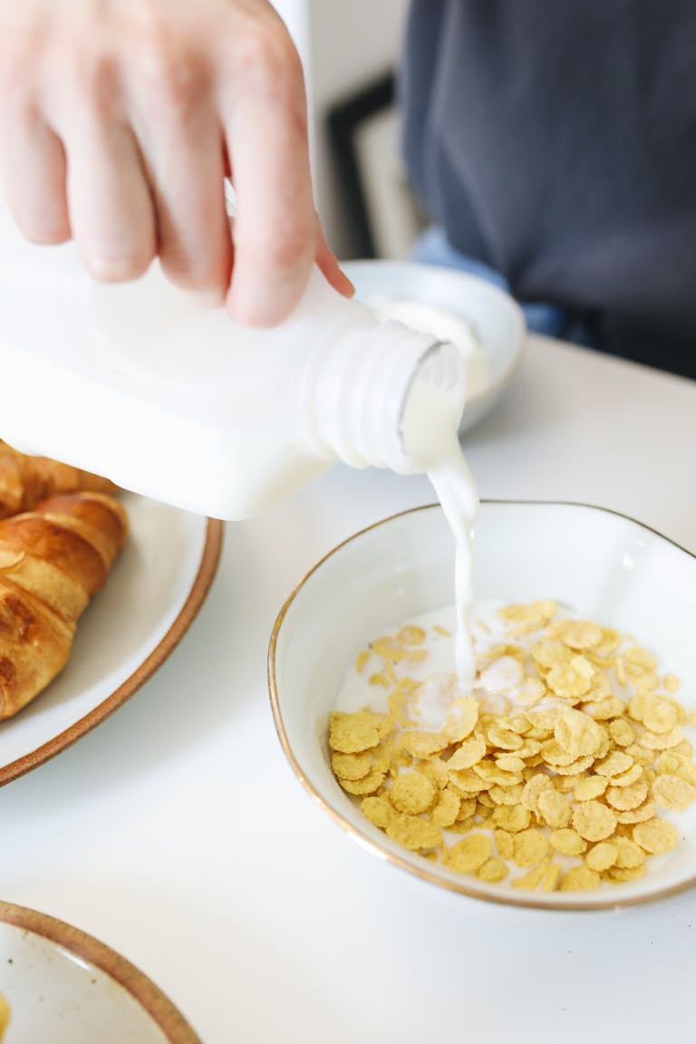 Hand pouring milk into a bowl of cereal for a breakfast setting.