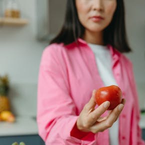 A person holding a fresh tomato over a bowl of assorted vegetables in a kitchen setting.