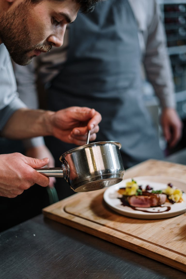 Chef adding final touches with sauce to a gourmet dish in a professional kitchen setting.