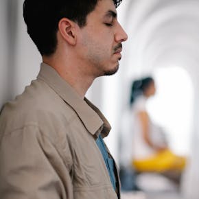 Side view of a man meditating indoors, focusing on relaxation and mindfulness.