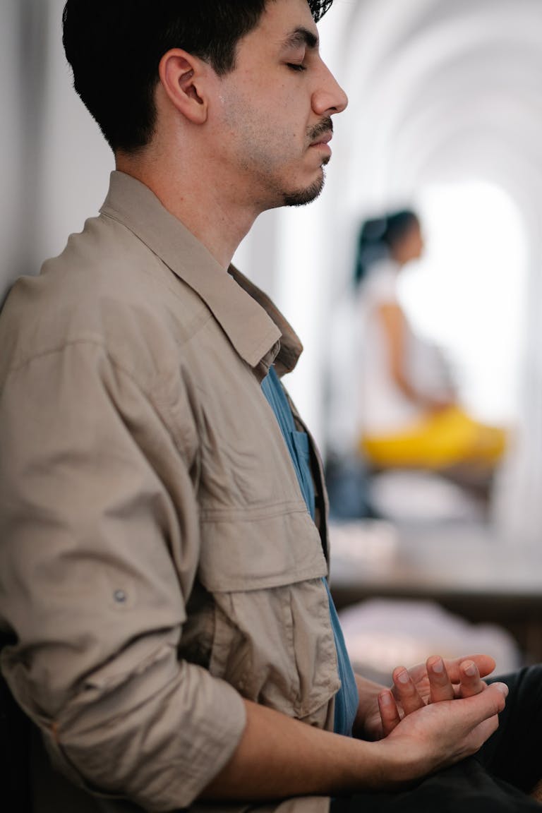Side view of a man meditating indoors, focusing on relaxation and mindfulness.