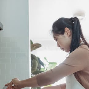 An Asian woman prepares a meal in a bright, modern kitchen. Indoor setting with a focus on home cooking.