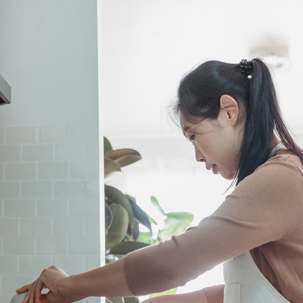 An Asian woman prepares a meal in a bright, modern kitchen. Indoor setting with a focus on home cooking.