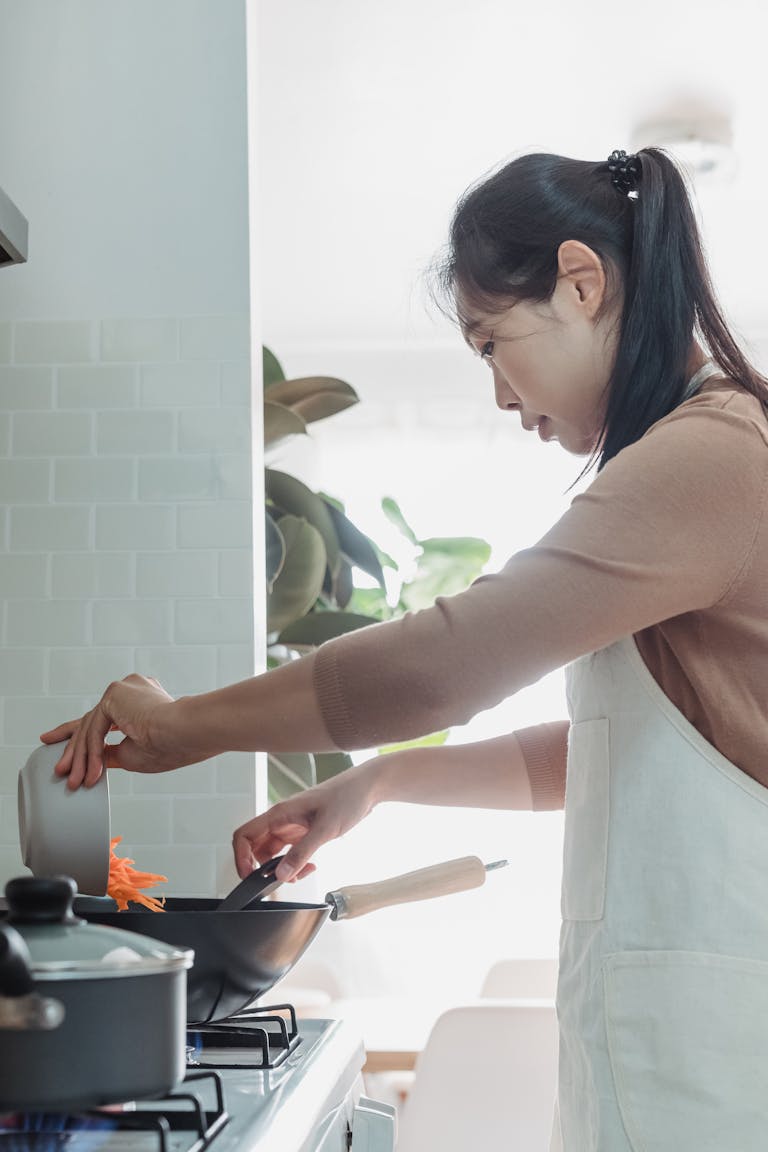 An Asian woman prepares a meal in a bright, modern kitchen. Indoor setting with a focus on home cooking.